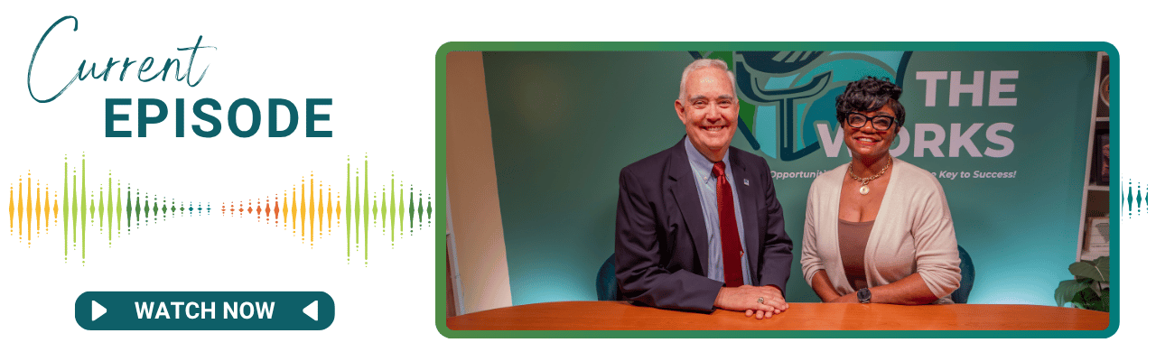 Two people sit at a table, a man and a women. Both are smiling. There is the Works logo behind them.